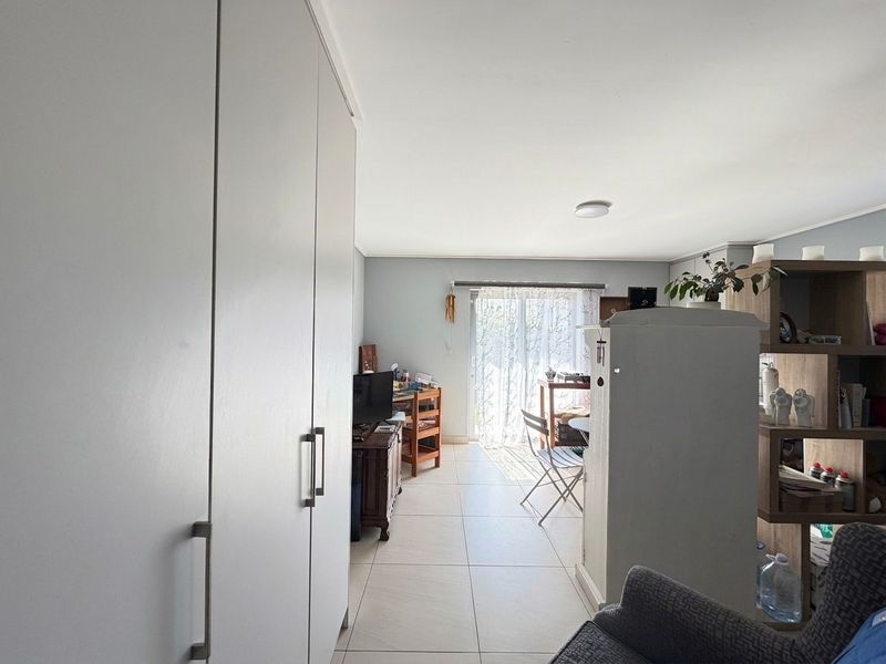Open-plan living area featuring neutral tiled flooring, built-in storage cupboards, and a sliding glass door providing access to the exterior.