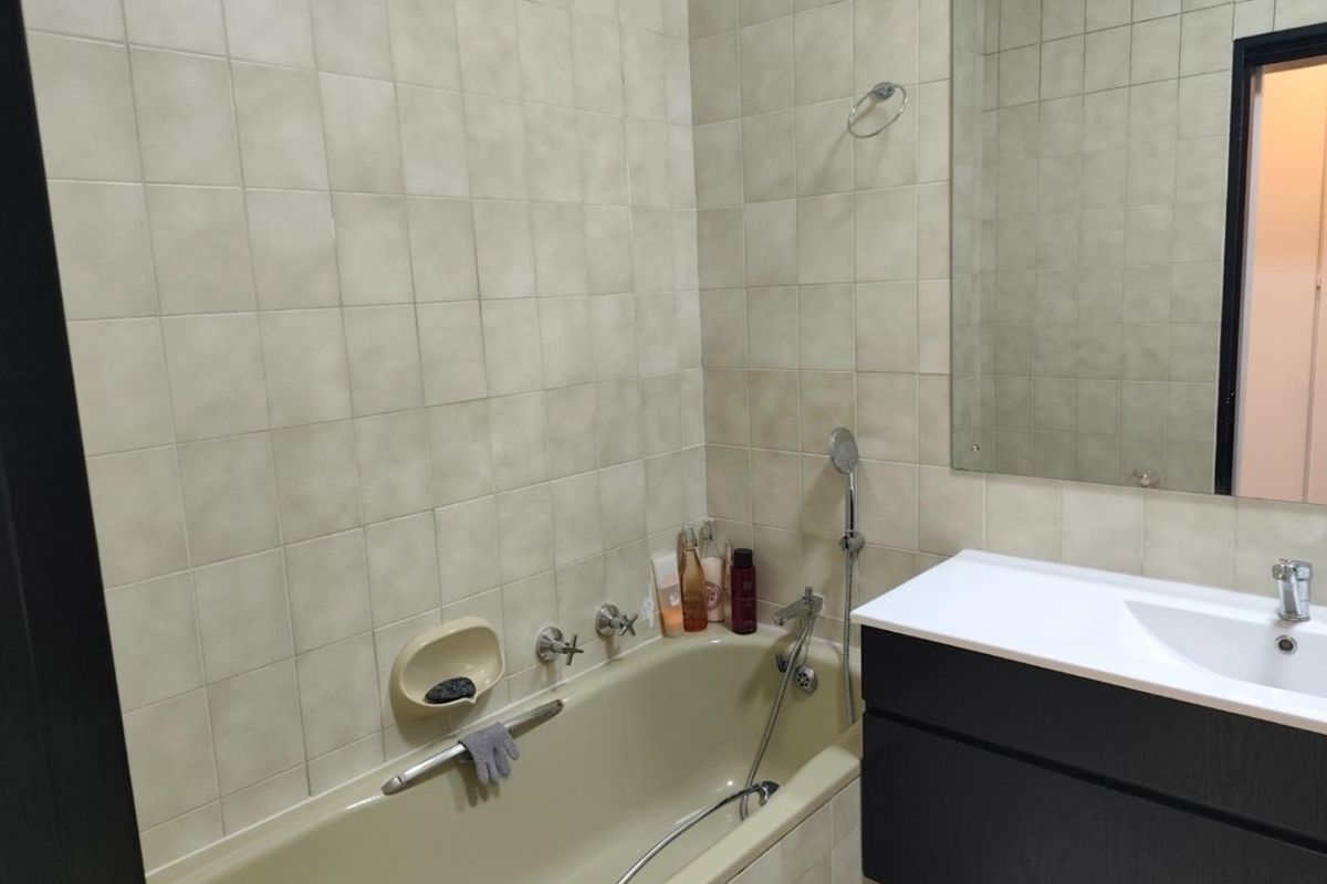 A functional bathroom featuring a bathtub with shower attachment, a modern vanity unit with integrated sink, and neutral wall tiling.