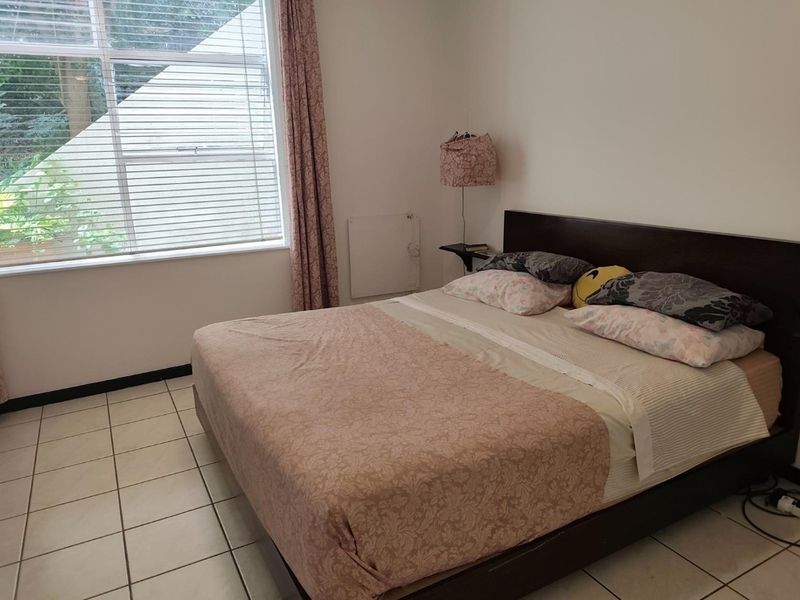 A bedroom featuring tiled flooring, a large window with blinds, and a wall-mounted heater.