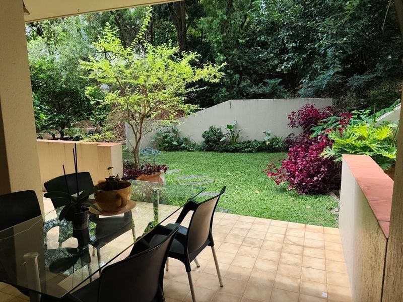 A covered patio area featuring tiled flooring, overlooking a private garden with established landscaping and a retaining wall.