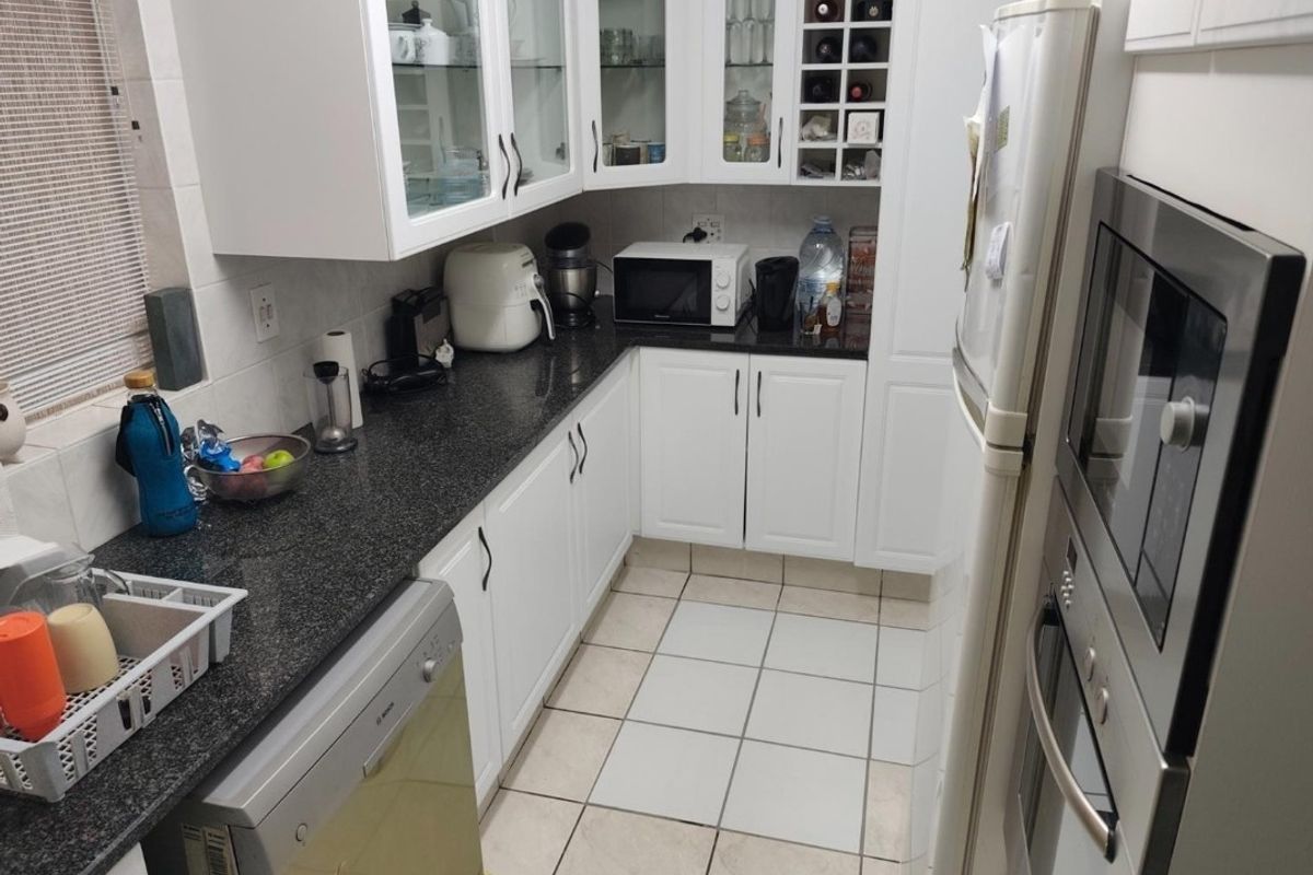 A functional kitchen featuring white shaker cabinetry, granite countertops, built-in oven, and tiled flooring, offering ample storage and a classic aesthetic.
