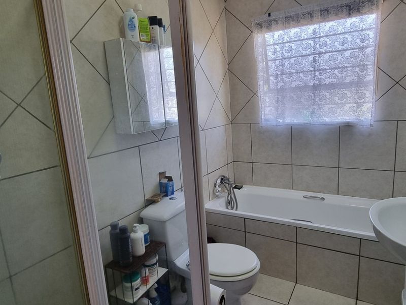 A functional bathroom featuring a shower enclosure, bathtub, pedestal basin, and toilet with neutral wall and floor tiling.