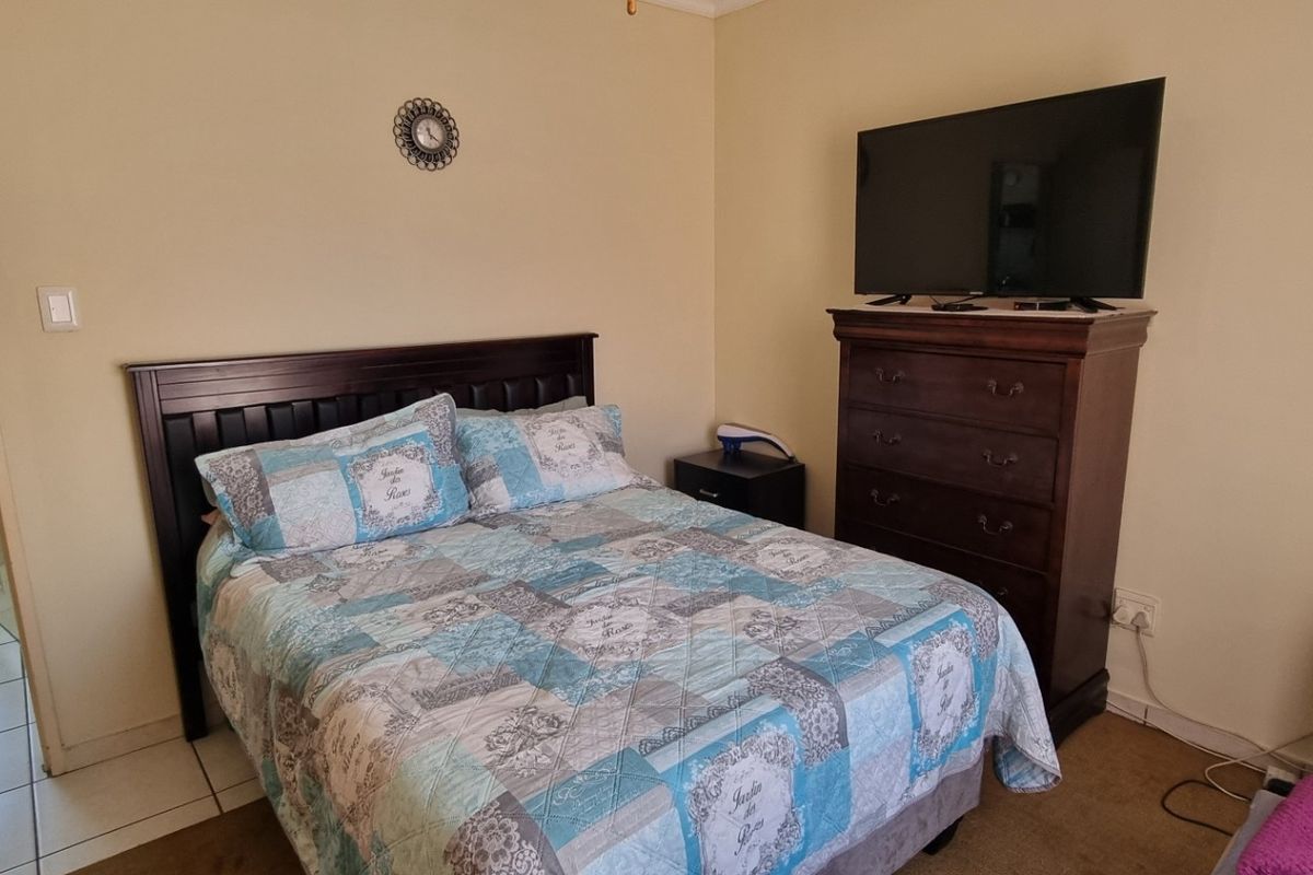 A functional bedroom featuring built-in wardrobe storage, neutral wall finishes, and direct access to an adjoining en-suite bathroom with tiled flooring.