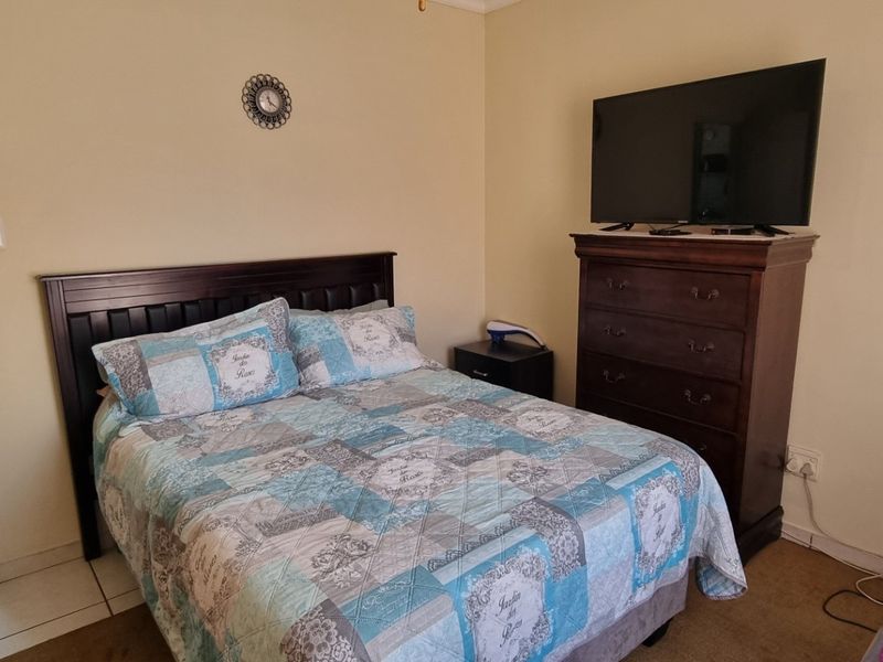 A functional bedroom featuring built-in wardrobe storage, neutral wall finishes, and direct access to an adjoining en-suite bathroom with tiled flooring.
