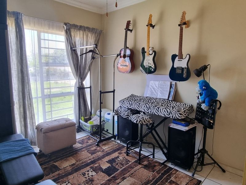 A bedroom featuring tiled flooring, a built-in cupboard, and a window fitted with security bars, currently utilized as a music practice space.