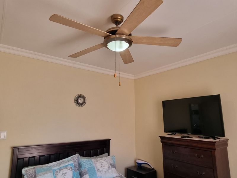 A bedroom featuring a ceiling fan, built-in cupboards, and coving, with an adjacent bathroom visible through the doorway.