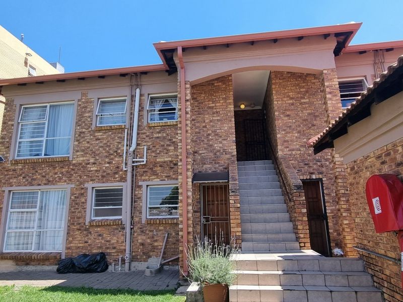 Rear view of a face brick townhouse complex featuring a tiled staircase, security gates, and paved courtyard area.