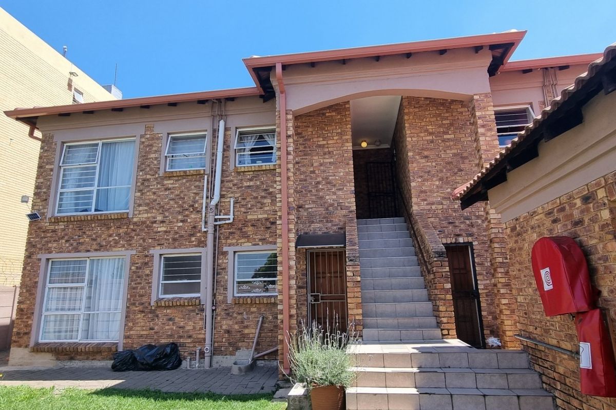 Rear view of a face brick townhouse complex featuring a tiled staircase, security gates, and paved courtyard area.
