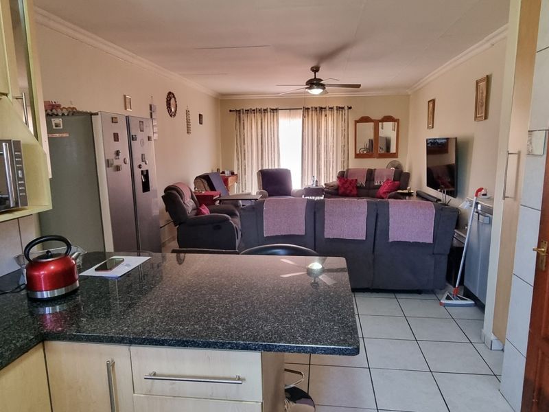 Open-plan living area featuring a kitchen with granite countertops and tiled flooring, flowing into a comfortable lounge space with a ceiling fan.