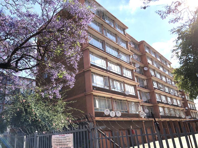 Exterior view of a multi-story apartment building featuring a brick facade, large windows, and security fencing with razor wire.