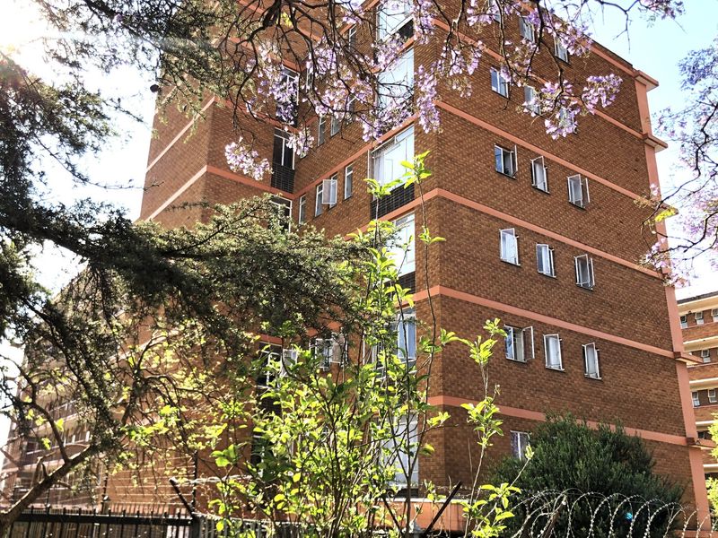 A multi-story apartment building featuring a face brick facade, casement windows, and perimeter security fencing with razor wire.