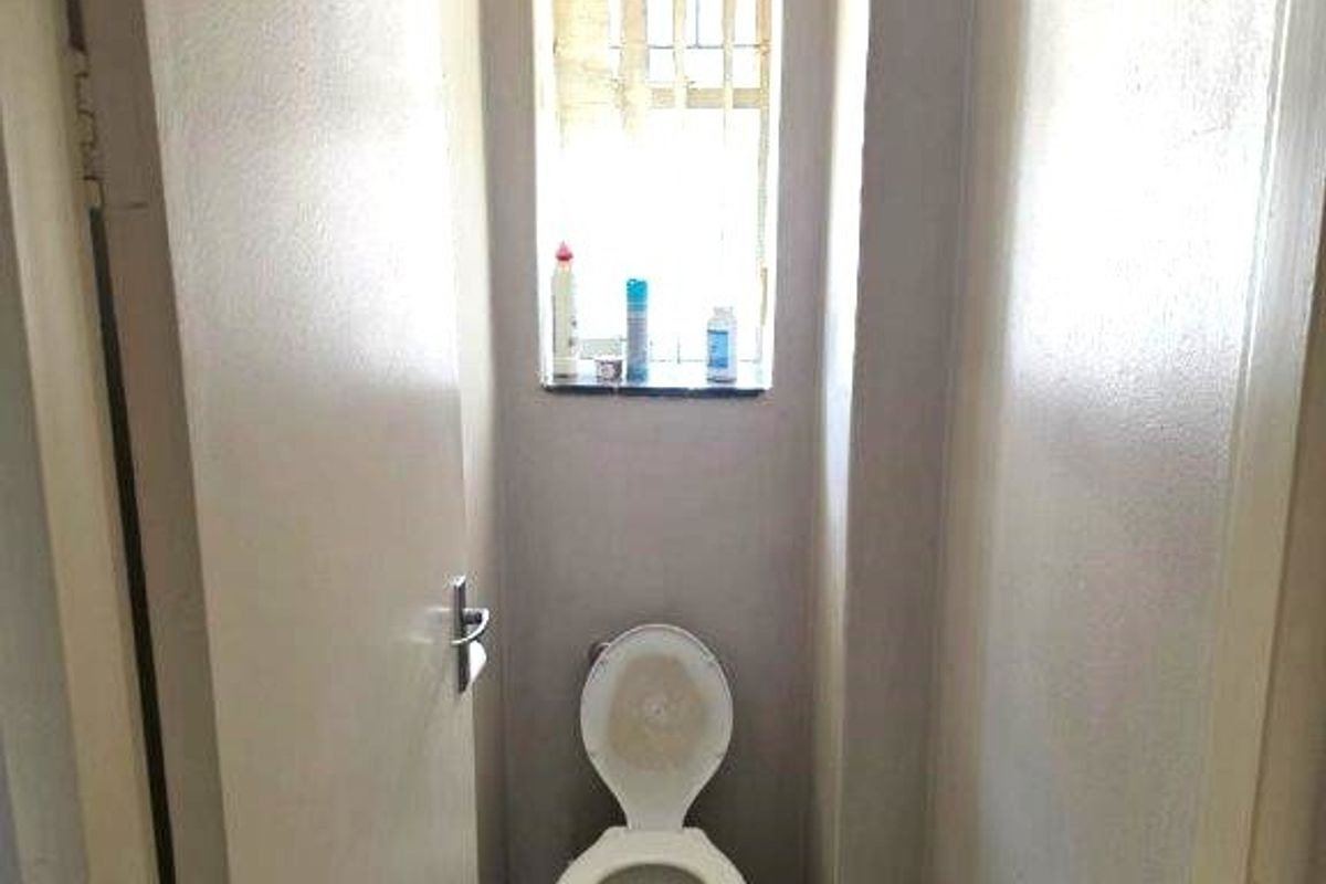 A compact, functional guest toilet featuring tiled flooring and a window with security bars, offering a basic layout ready for modernization.