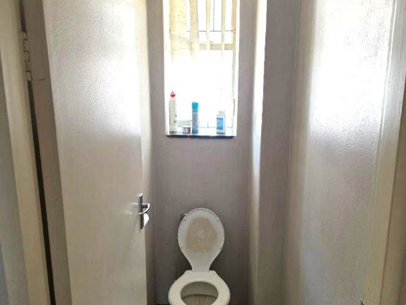 A compact, functional guest toilet featuring tiled flooring and a window with security bars, offering a basic layout ready for modernization.