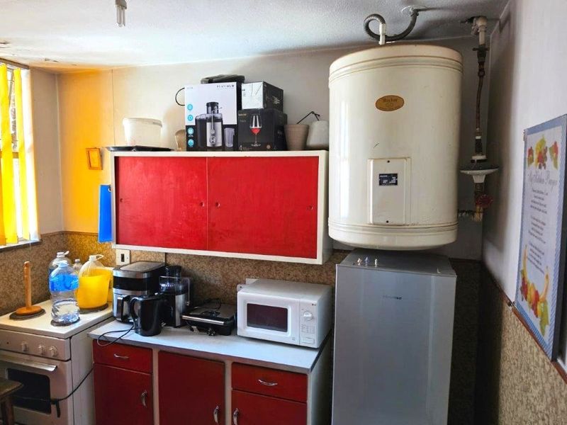 A compact kitchen area featuring red cabinetry, a built-in electric stove, and a wall-mounted electric water heater.