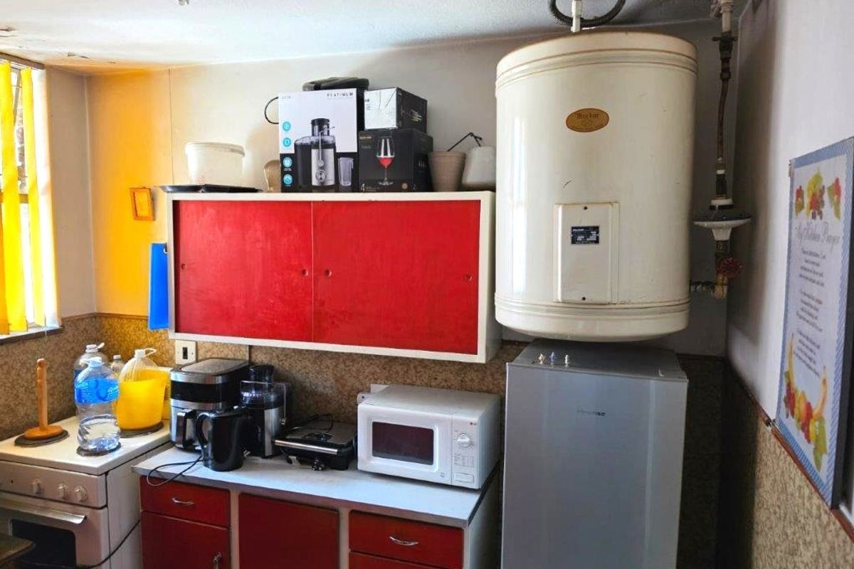 A compact kitchen area featuring red cabinetry, a built-in electric stove, and a wall-mounted electric water heater.