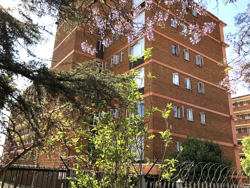 Exterior view of a multi-story apartment building featuring a face brick facade, steel windows, and perimeter security fencing with razor wire.