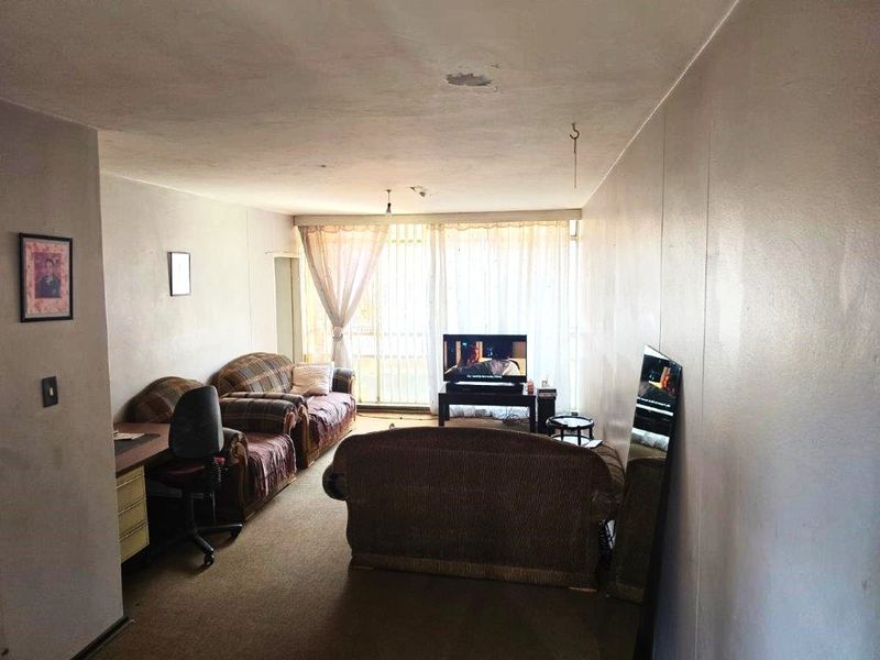 A living room area featuring carpet flooring and a sliding glass door leading to a balcony, currently showing signs of wear and ceiling damage.