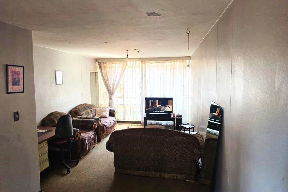 A living room area featuring carpet flooring and a sliding glass door leading to a balcony, currently showing signs of wear and ceiling damage.