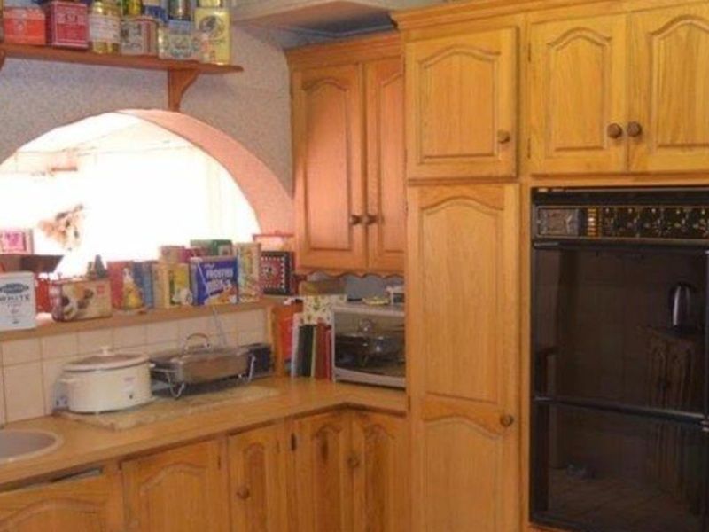 A dated kitchen featuring traditional wooden cabinetry, a built-in oven, and a distinctive arched opening, offering significant potential for a modern renovation.