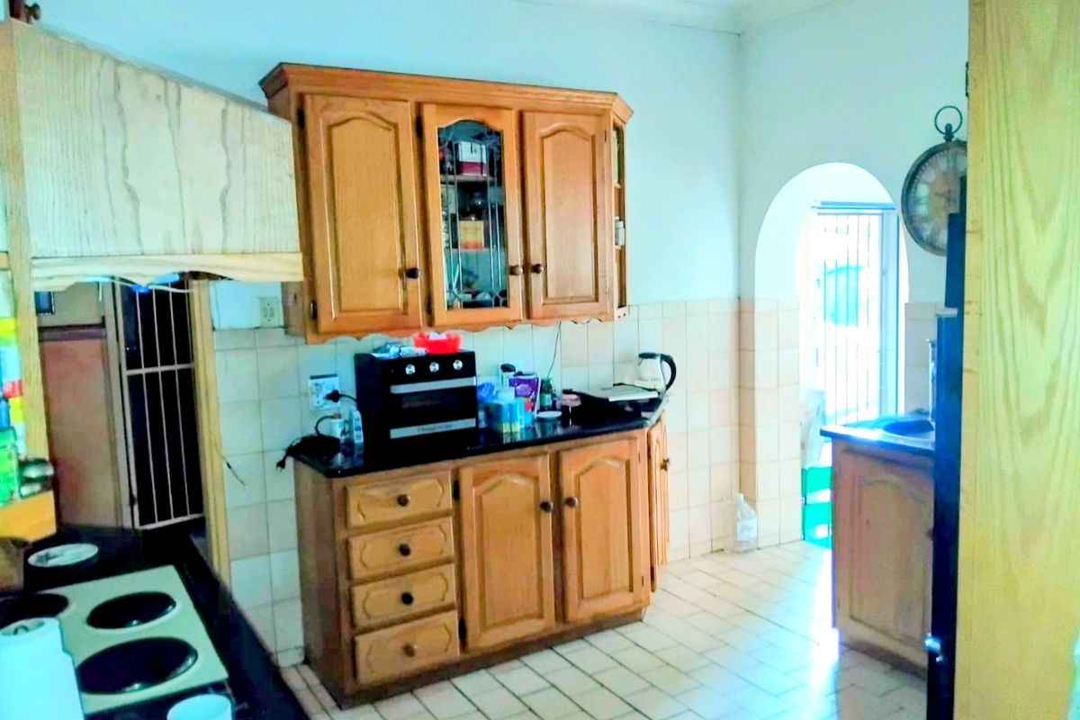 A functional kitchen featuring wooden cabinetry, tiled flooring, and a classic archway leading to an adjacent area, offering potential for modern updates.