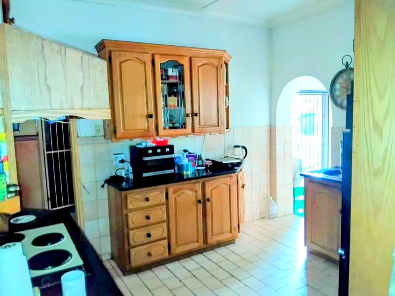 A functional kitchen featuring wooden cabinetry, tiled flooring, and a classic archway leading to an adjacent area, offering potential for modern updates.