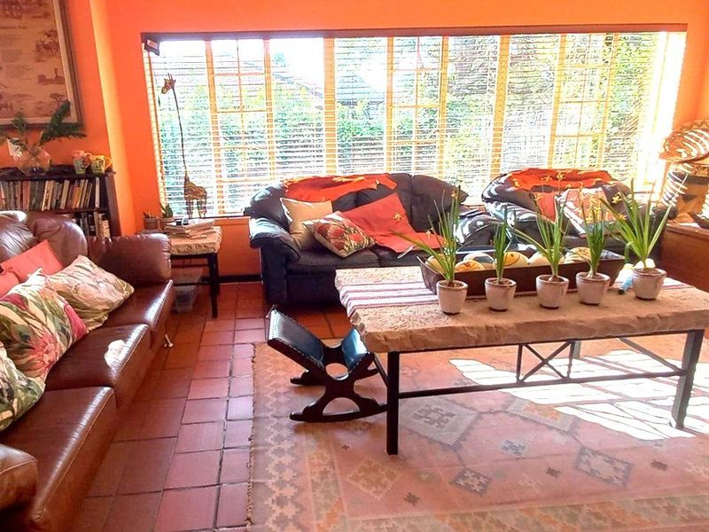 A sunlit living room featuring terracotta floor tiles and a large bank of windows with venetian blinds, offering a warm and inviting atmosphere.