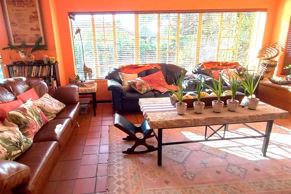 A sunlit living room featuring terracotta floor tiles and a large bank of windows with venetian blinds, offering a warm and inviting atmosphere.