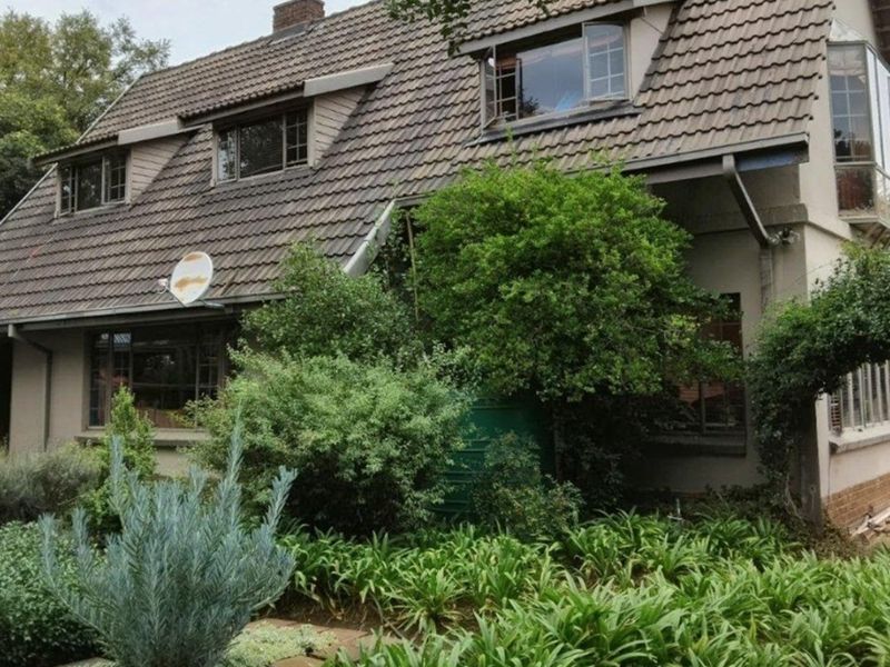 A two-story residential home featuring a tiled roof, dormer windows, and established garden landscaping.
