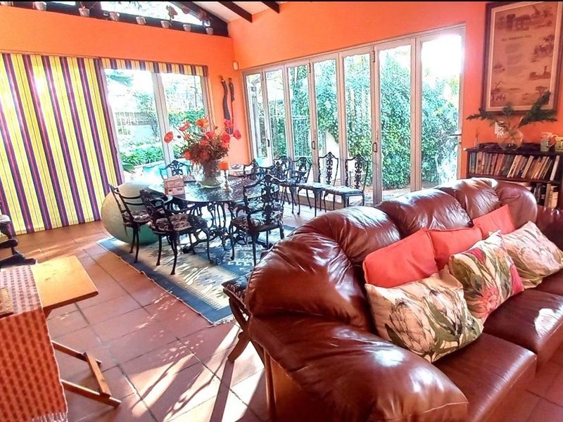 Spacious open-plan living and dining area featuring terracotta flooring, exposed timber ceiling beams, and extensive glass doors providing natural light and garden access.
