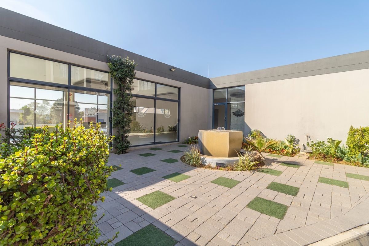 A modern paved courtyard featuring a central water feature, landscaped garden beds, and large glass sliding doors providing access to the interior.