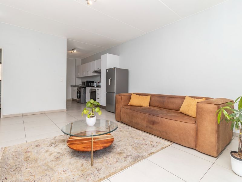 An open-plan living area featuring tiled floors and a compact kitchen with built-in cabinetry, oven, and hob, creating a functional and connected living space.