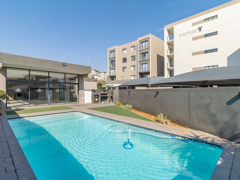 Communal pool area featuring a well-maintained swimming pool, paved surround, artificial lawn, and modern shade sails within an apartment complex.