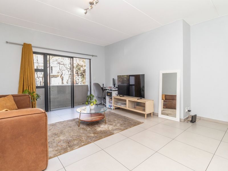 A bright living room featuring neutral tiled flooring and a large sliding glass door providing access to an outdoor balcony area.