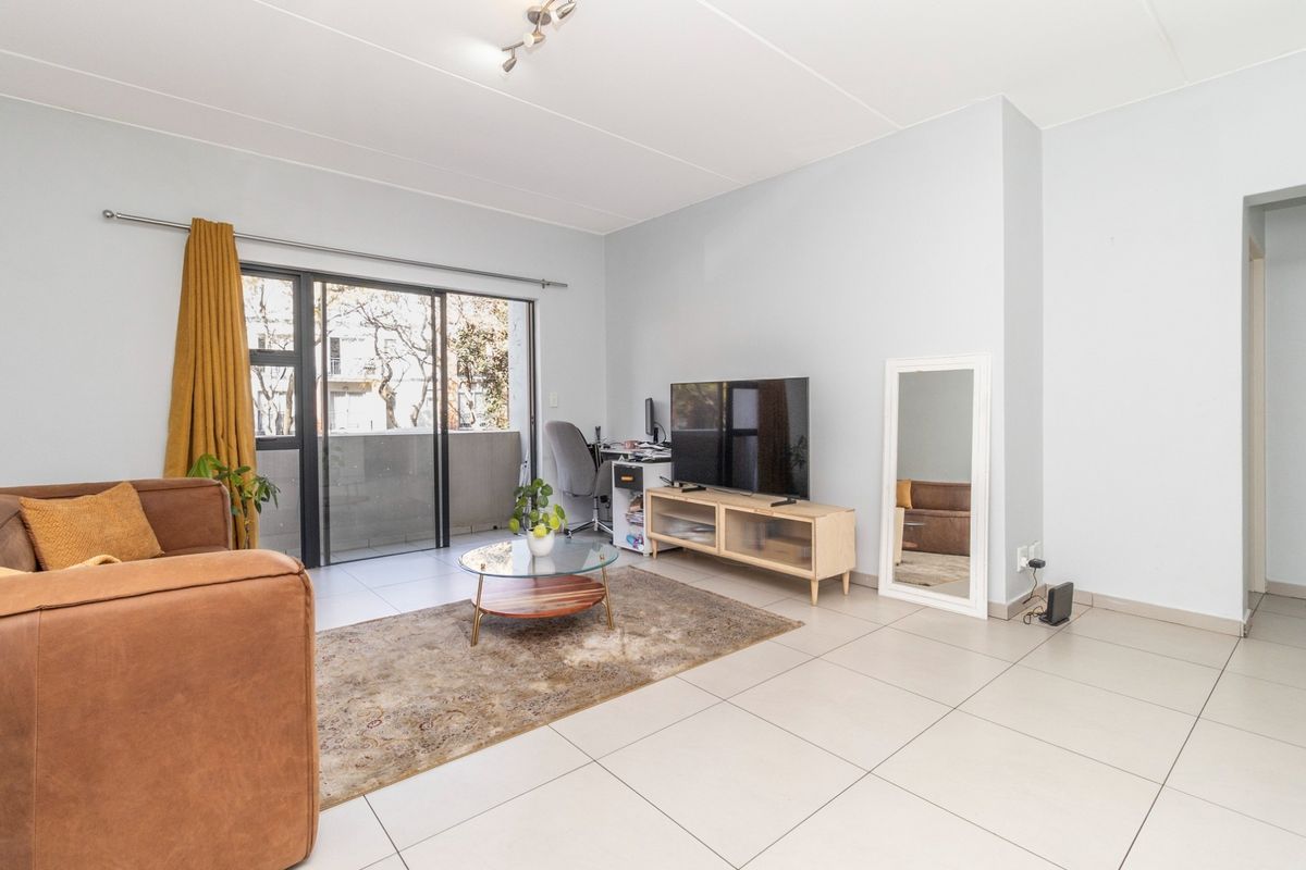 A bright living room featuring neutral tiled flooring and a large sliding glass door providing access to an outdoor balcony area.