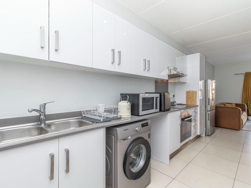 Modern galley-style kitchen featuring white cabinetry, stone countertops, integrated oven, extractor fan, and tiled flooring, seamlessly flowing into the adjacent living area.