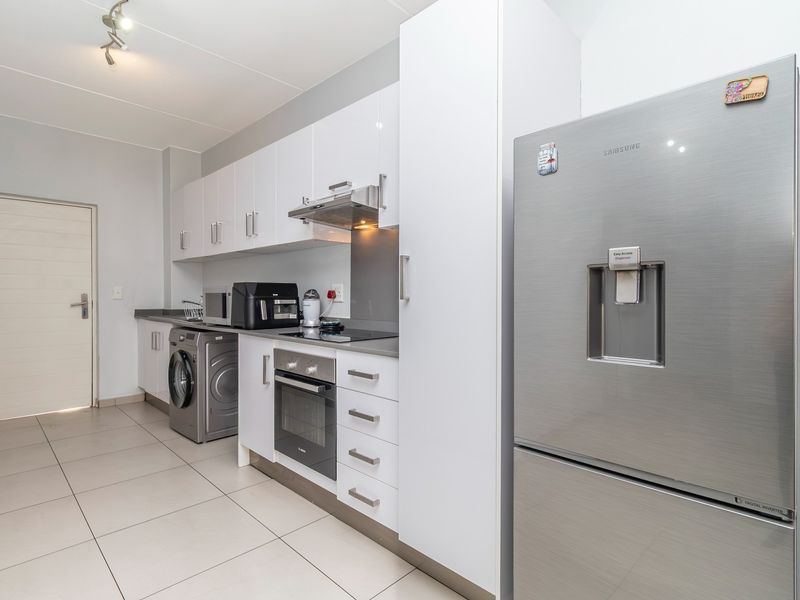 Modern kitchen featuring white cabinetry, integrated oven, electric hob, extractor fan, and tiled flooring, offering a clean and functional workspace.