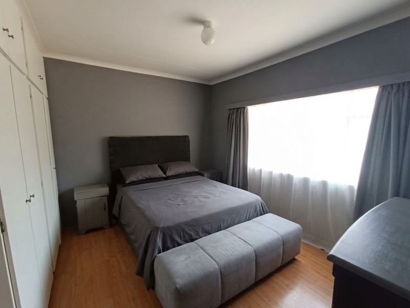 A well-maintained bedroom featuring laminate flooring, neutral grey walls, and ample built-in cupboard storage space.