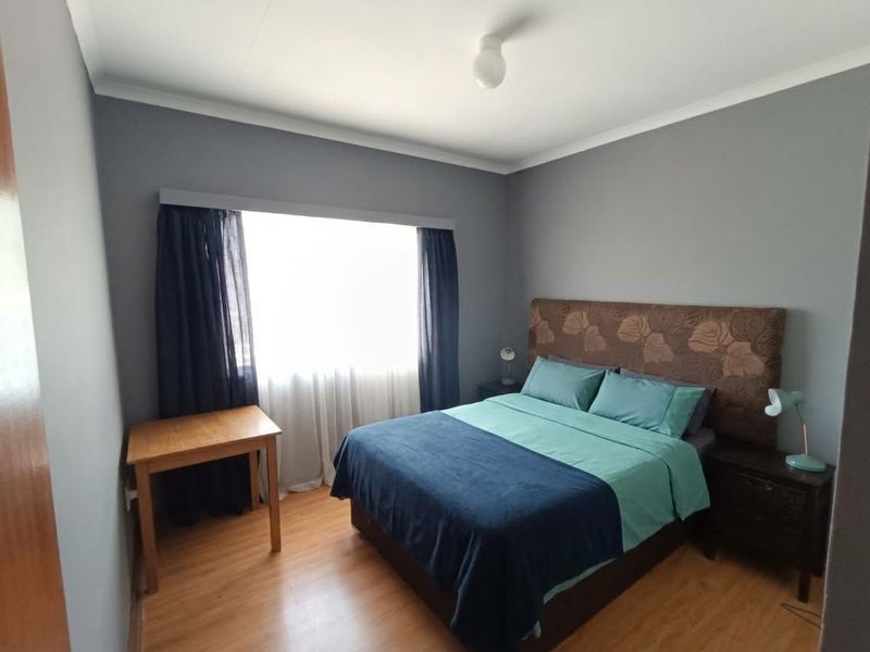 A standard bedroom featuring laminate flooring, grey painted walls, and a window with a fitted curtain rail.