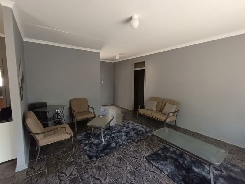 A spacious living room featuring neutral grey walls, tiled flooring, and simple ceiling lighting, offering a clean and functional space for relaxation.