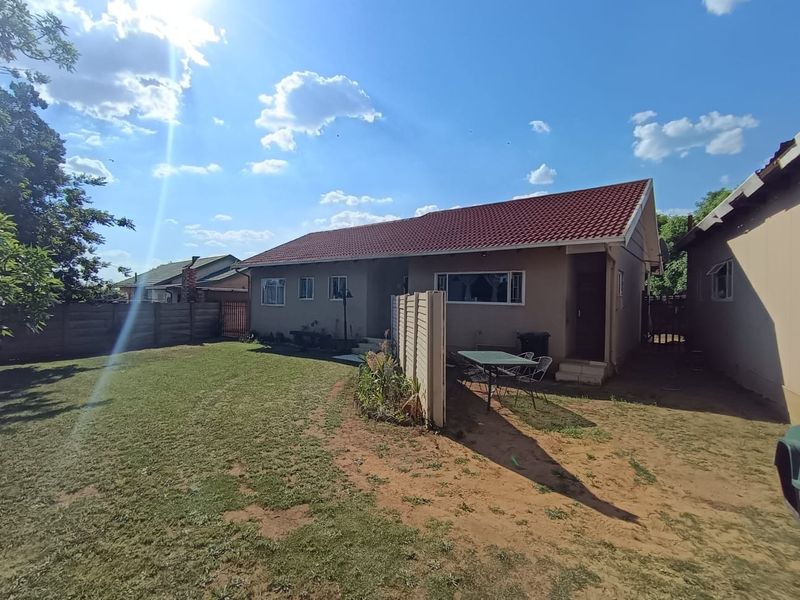 Rear view of the house featuring a tiled roof, exterior wall finishes, and a spacious backyard with a boundary wall.