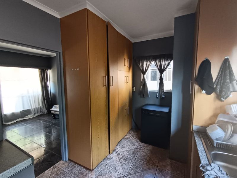 A functional scullery area featuring built-in wooden cabinetry, tiled flooring, and a double sink, providing additional prep and storage space adjacent to the main living area.