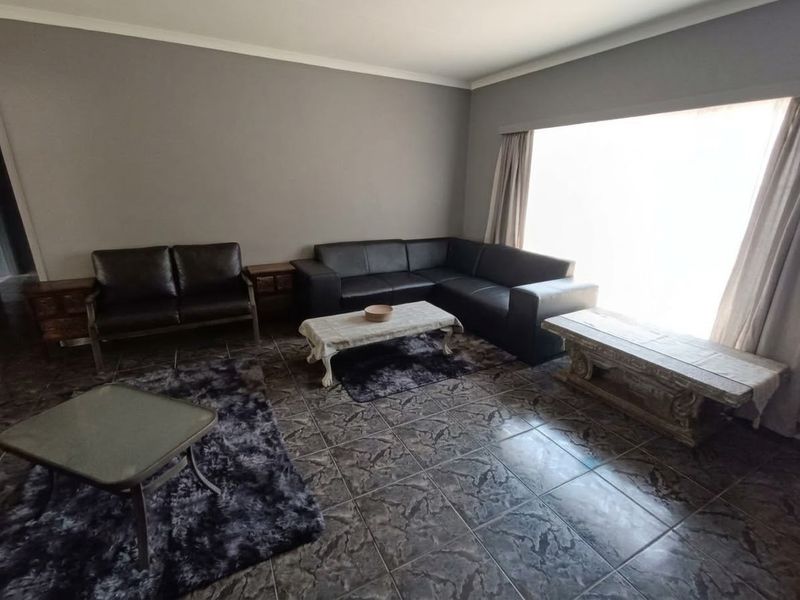 A spacious living room featuring dark tiled flooring, neutral wall tones, and a large window allowing for ample natural light.