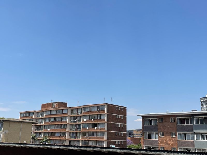 An exterior view of neighbouring apartment buildings featuring brick facades and standard window configurations under a clear blue sky.