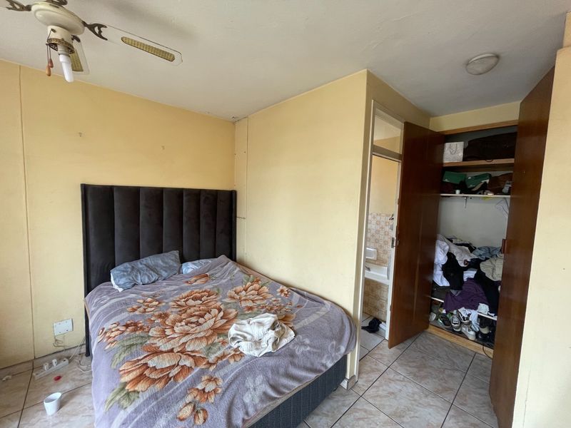 A bedroom featuring tiled flooring, a ceiling fan, and a built-in wardrobe, with an adjacent bathroom visible through the doorway.