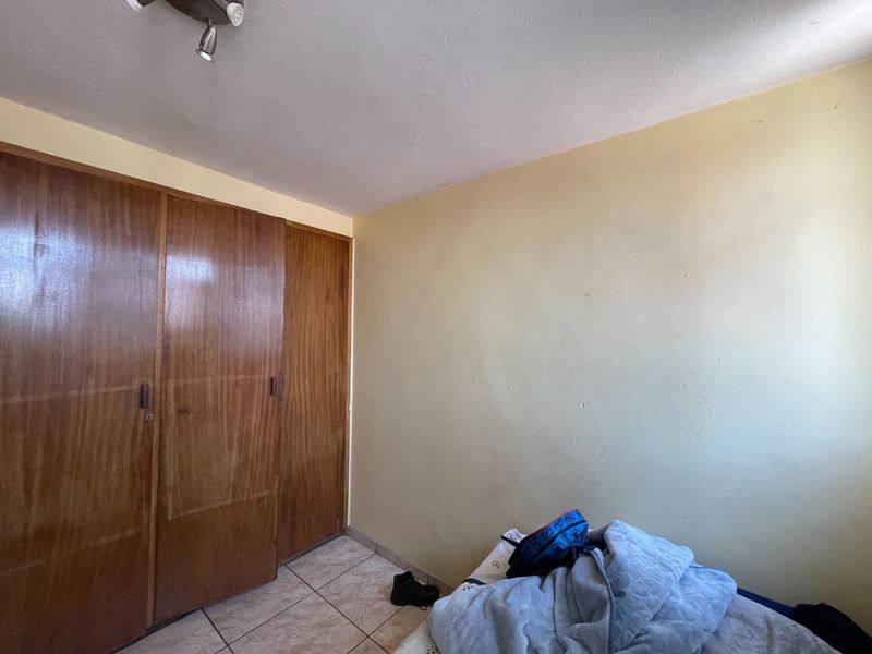 A bedroom featuring built-in wooden wardrobes and tiled flooring, requiring some cosmetic updates to the wall finishes.