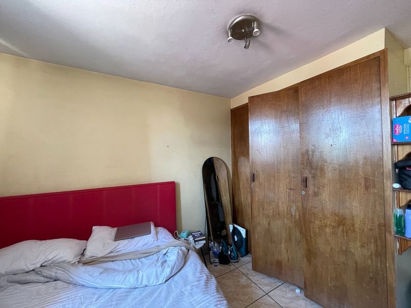 A bedroom featuring built-in wooden wardrobes, tiled flooring, and a ceiling light fixture. The room requires cosmetic updates to the wall finishes.