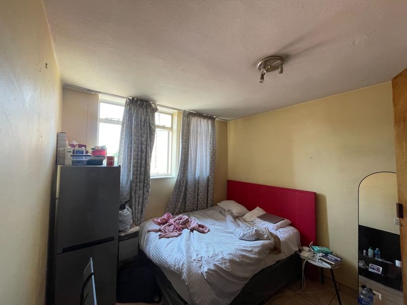 A bedroom featuring a window and ceiling light fixture, currently showing signs of wear on the wall surfaces.