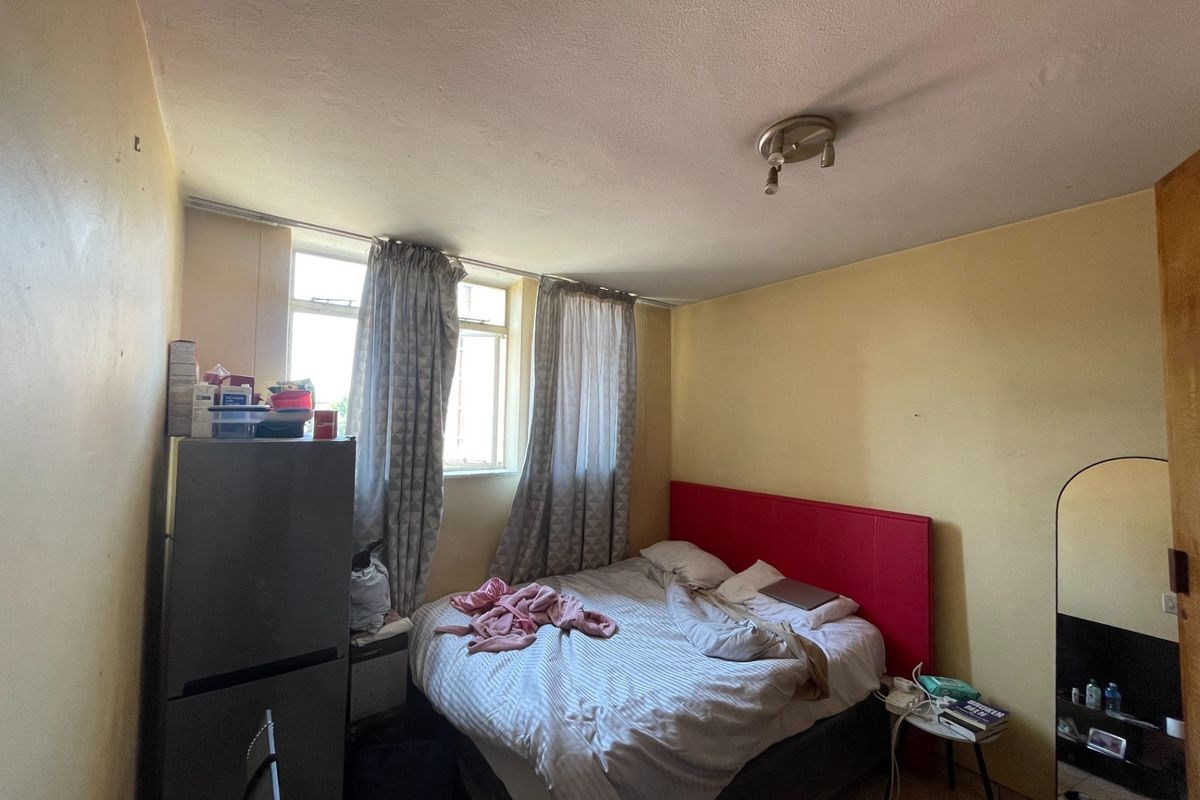 A bedroom featuring a window and ceiling light fixture, currently showing signs of wear on the wall surfaces.