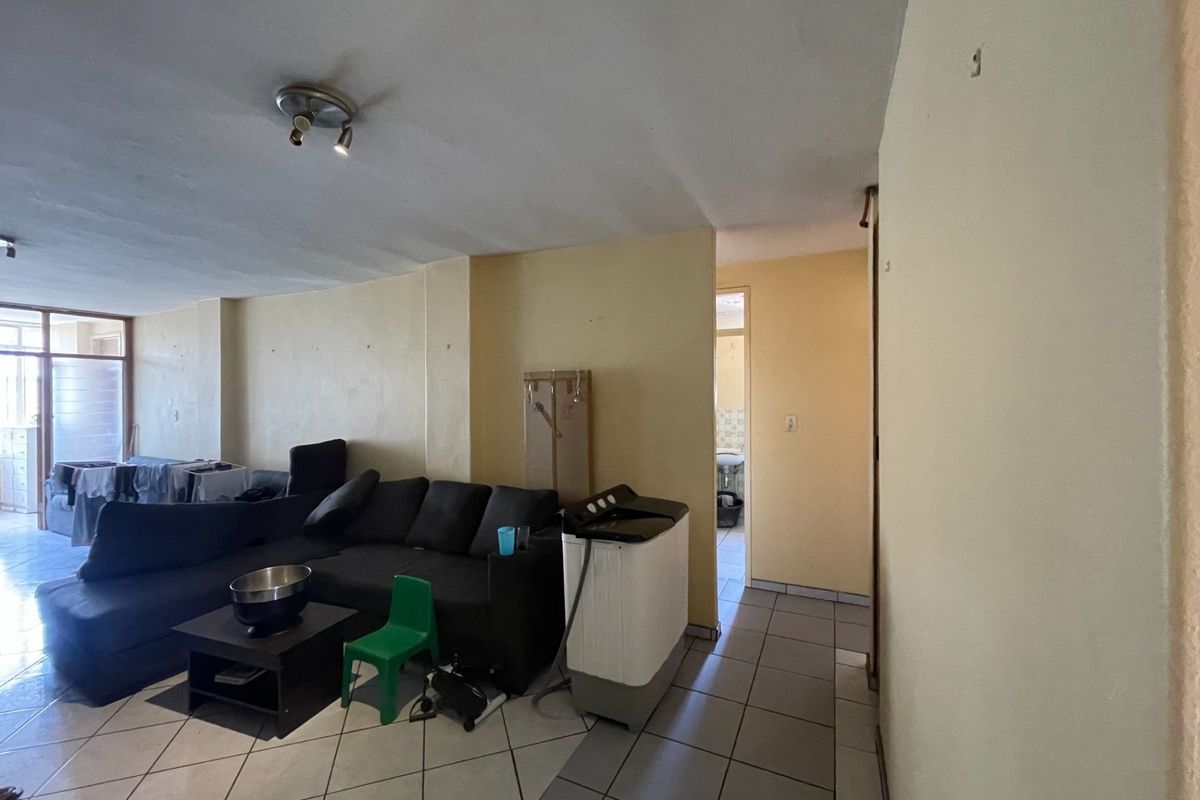 A living area featuring tiled flooring and neutral wall finishes, providing a functional space with direct access to adjacent rooms.