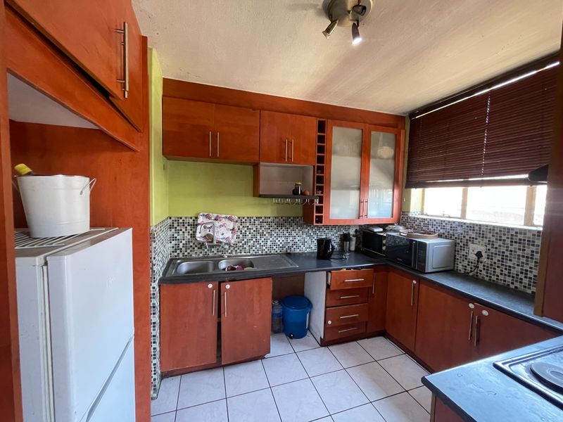 A functional kitchen featuring wooden cabinetry, mosaic tile backsplash, double basin sink, and ceramic floor tiles, offering potential for modernization.